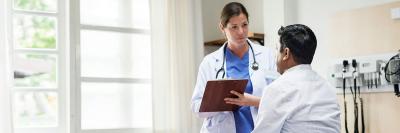 doctor writing on clipboard while talking to patient